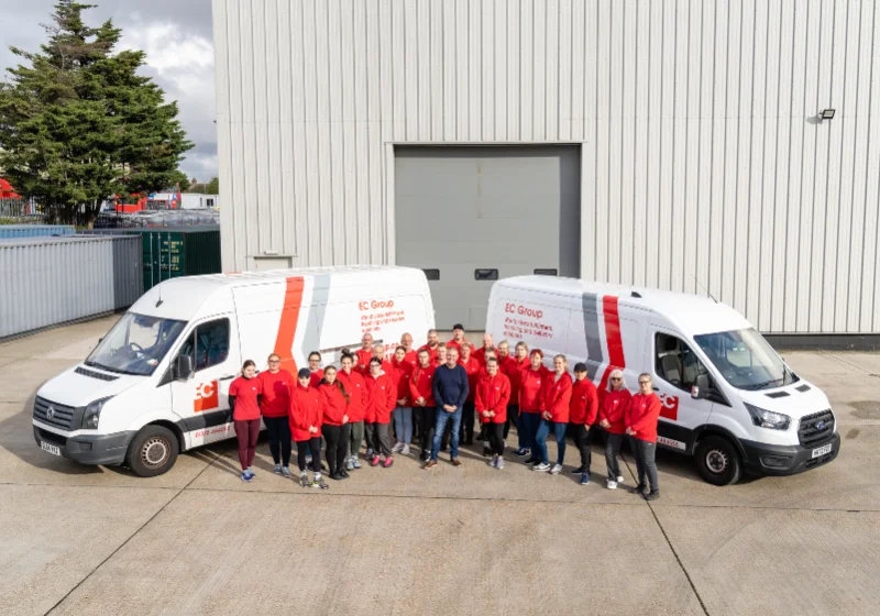 An image of the EC Group team alongside their fleet of vehicles, and their warehouse