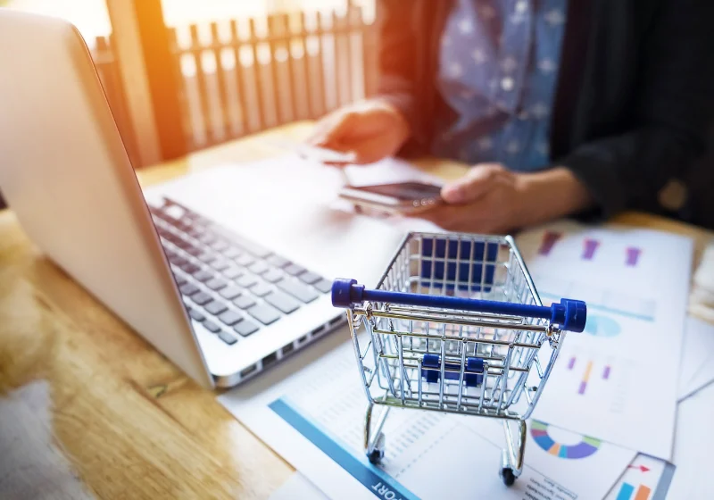 An image of a person using their phone near their laptop, a small toy trolley is alongside